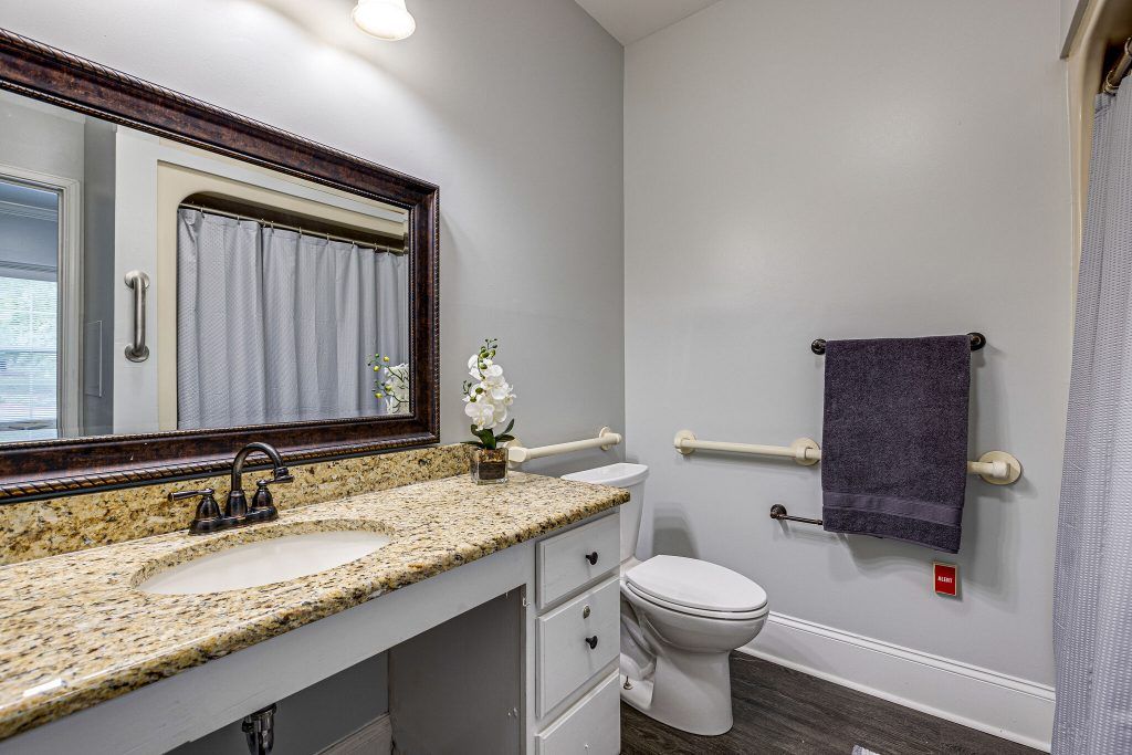 A modern bathroom with a granite countertop, mirror, and neatly arranged decor.