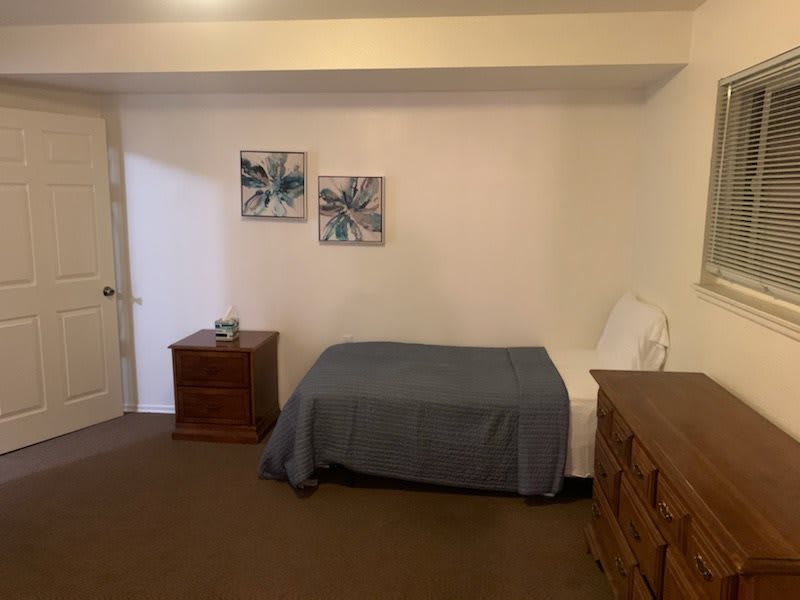 A minimalist bedroom with a single bed, wooden furniture, and wall art.