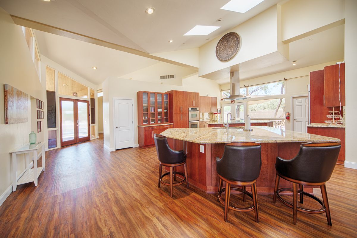 A spacious and modern kitchen interior featuring wood flooring, an island counter, and bar stools.