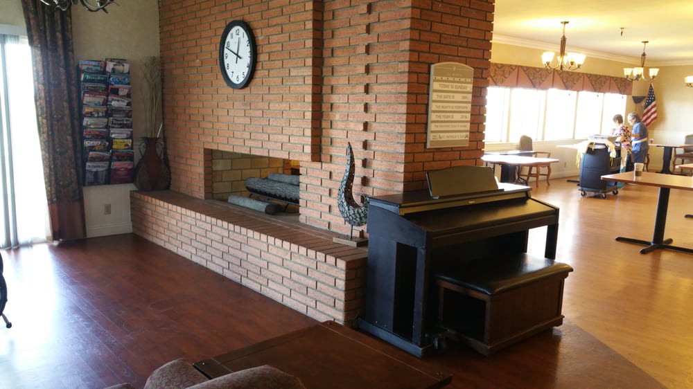 A cozy living room featuring a brick wall with a fireplace, clock, and piano.