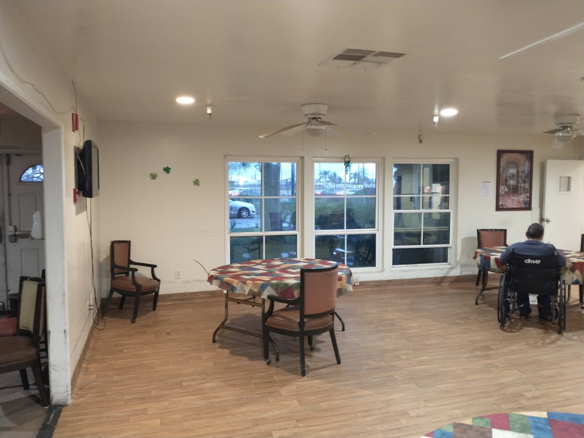 A well-lit dining area with tables and chairs, featuring large windows and a wood floor.