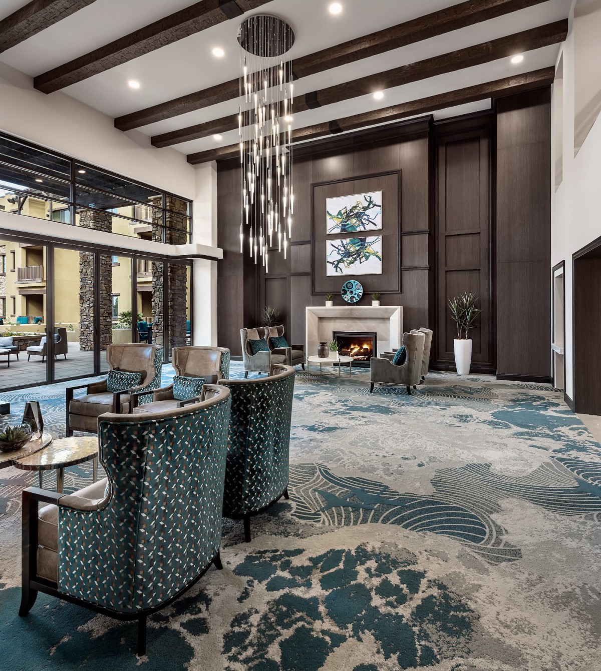 A modern and spacious lobby featuring a seating area, a central fireplace, and a stylish chandelier, with large windows providing ample natural light.