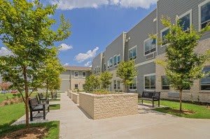 Modern building with a landscaped outdoor area and benches under a clear blue sky.