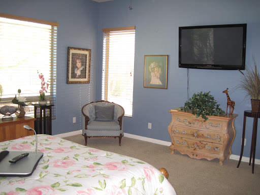 A cozy bedroom featuring a comfortable armchair, wall art, and a television mounted above the dresser.