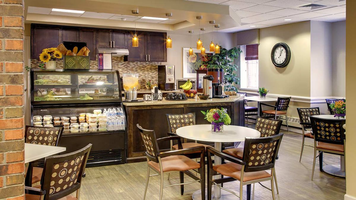 A cozy cafe interior featuring a seating area with tables and chairs, a coffee counter, and warm decor.
