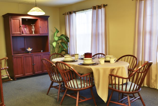A cozy dining room with a table set for a meal, surrounded by wooden chairs and a cabinet in the corner.
