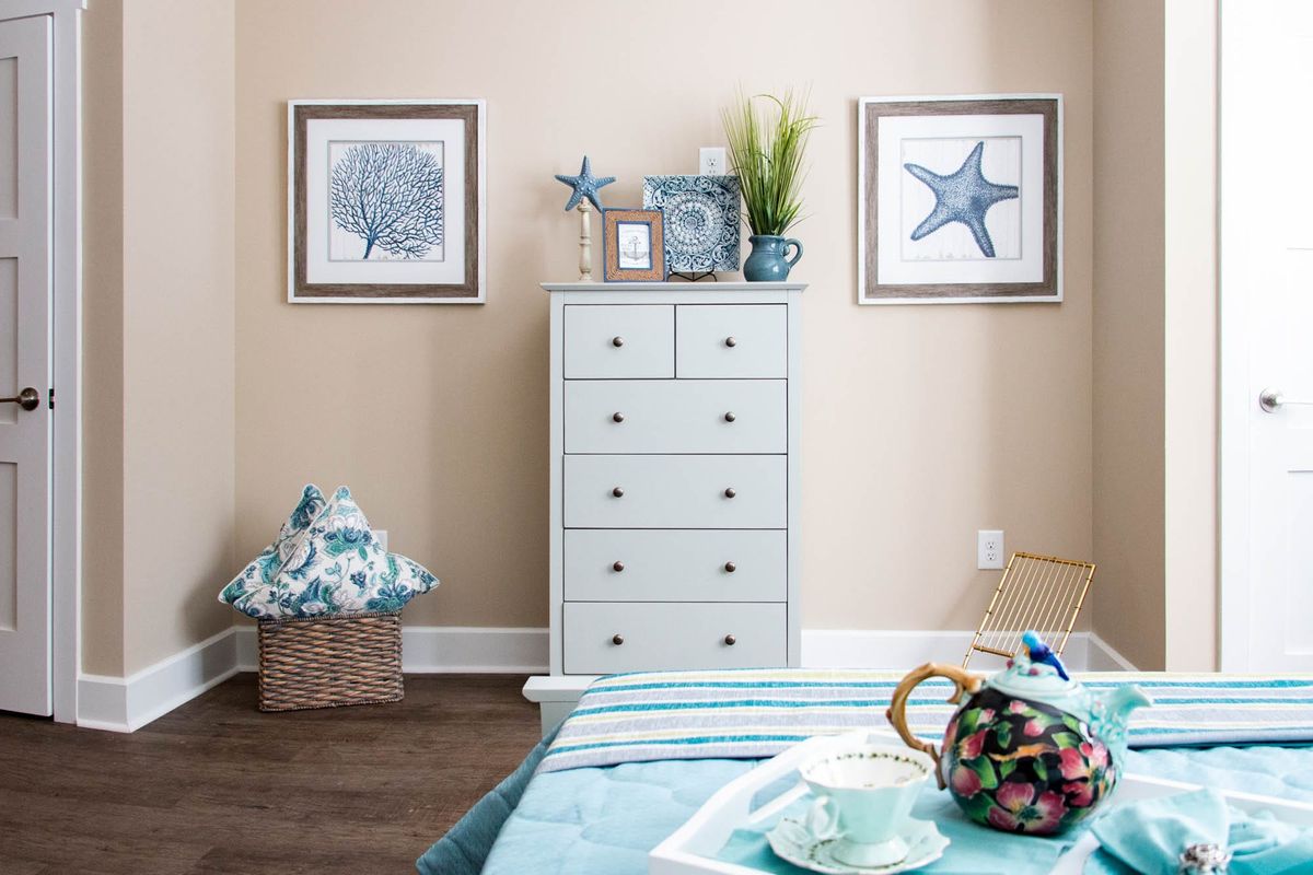 A cozy bedroom with coastal-themed decor featuring a dresser, starfish and shell artwork, and blue accents.