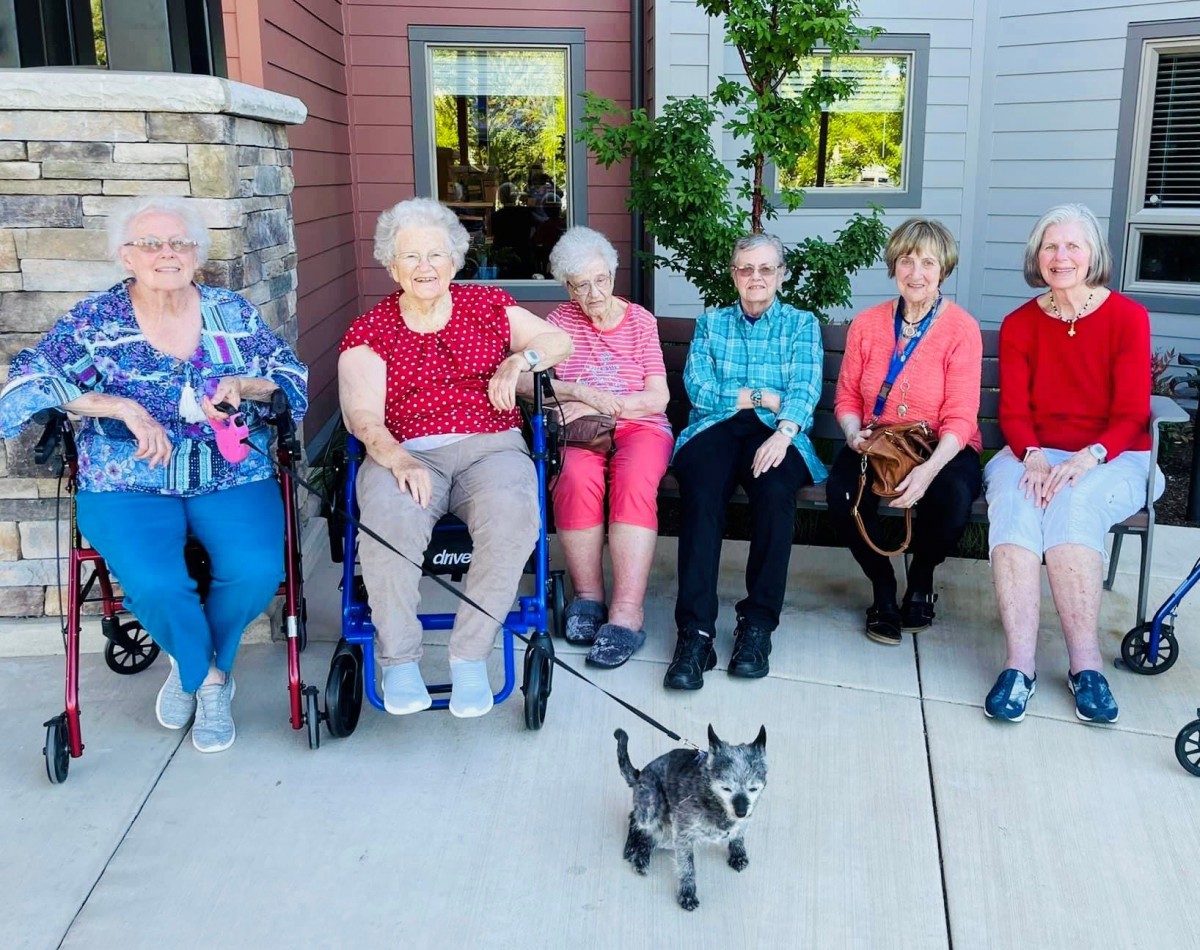 A group of seniors sitting outside with a small dog in front of them.