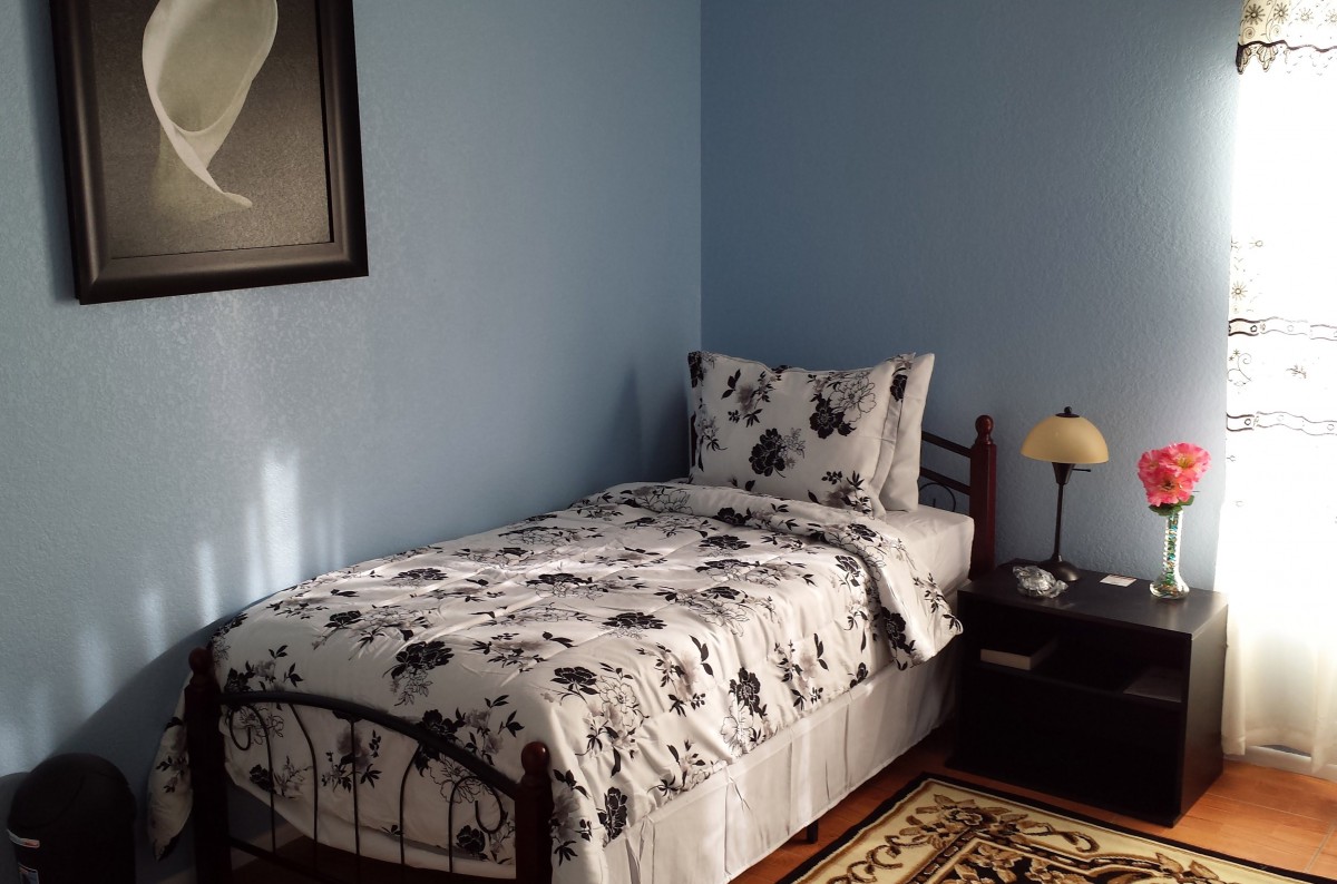 A cozy bedroom with a single bed, floral bedding, and blue walls.