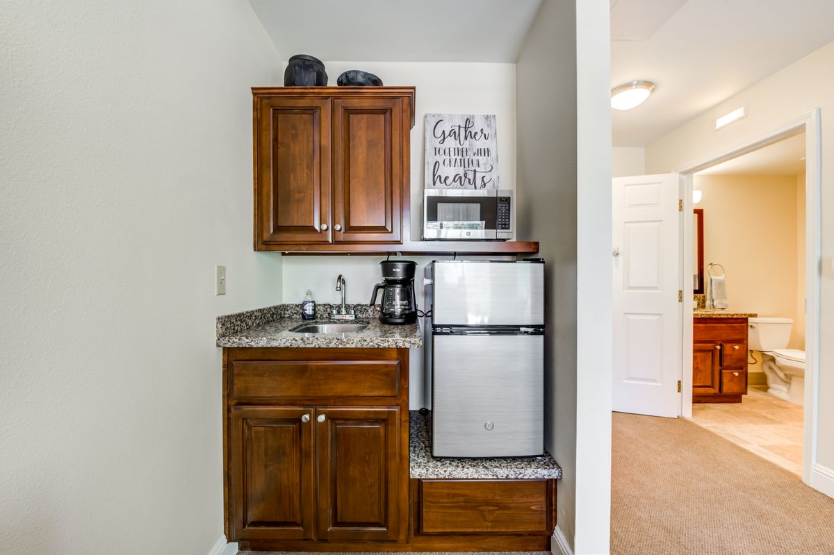 A compact kitchenette featuring a mini fridge, coffee maker, sink, and wooden cabinets.