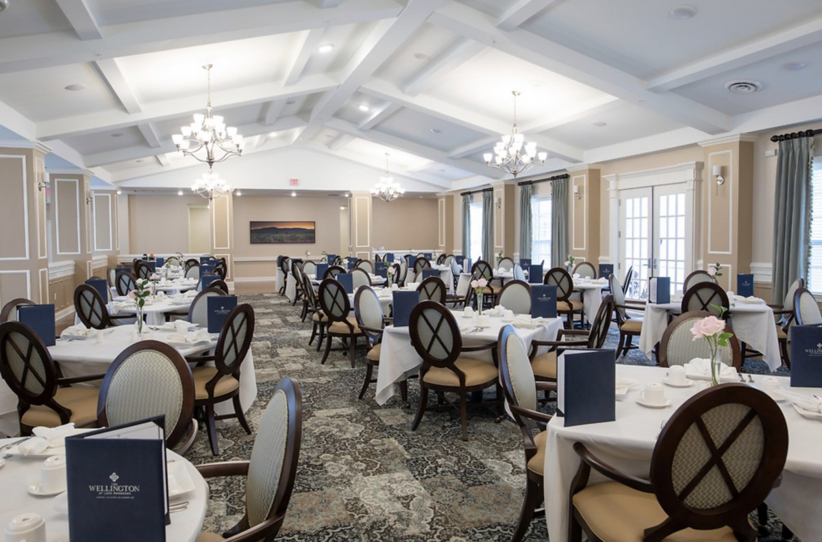 An elegant dining room with neatly arranged tables and chairs, illuminated by chandeliers.