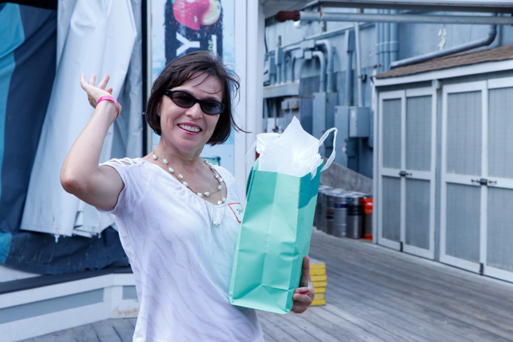 A woman wearing sunglasses is happily holding a shopping bag outdoors.