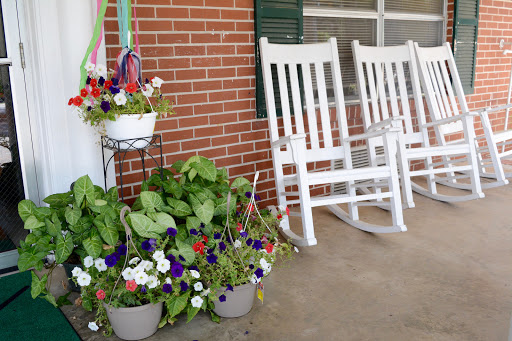 A cozy front porch featuring white rocking chairs and vibrant flower pots, perfect for relaxation.