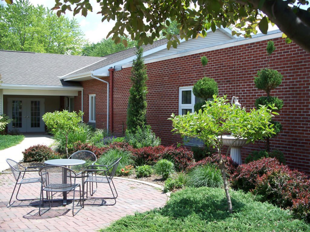 A serene garden patio with outdoor seating and lush greenery beside a brick building.