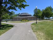 A sunny day in the park with a building and pathway surrounded by trees.