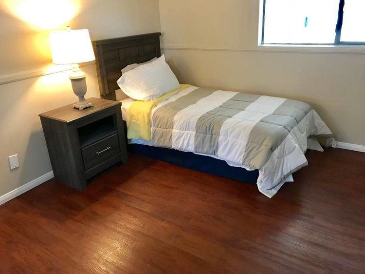 A cozy bedroom with a single bed, nightstand, and lamp on a hardwood floor.