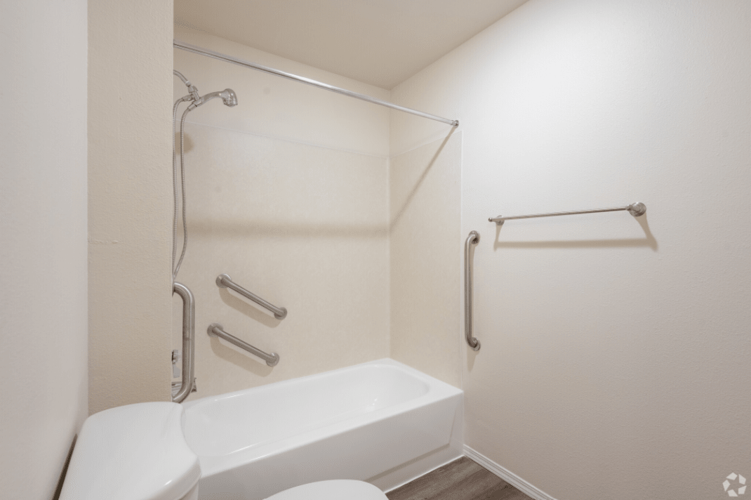 An accessible bathroom with a bathtub, shower, and grab bars.
