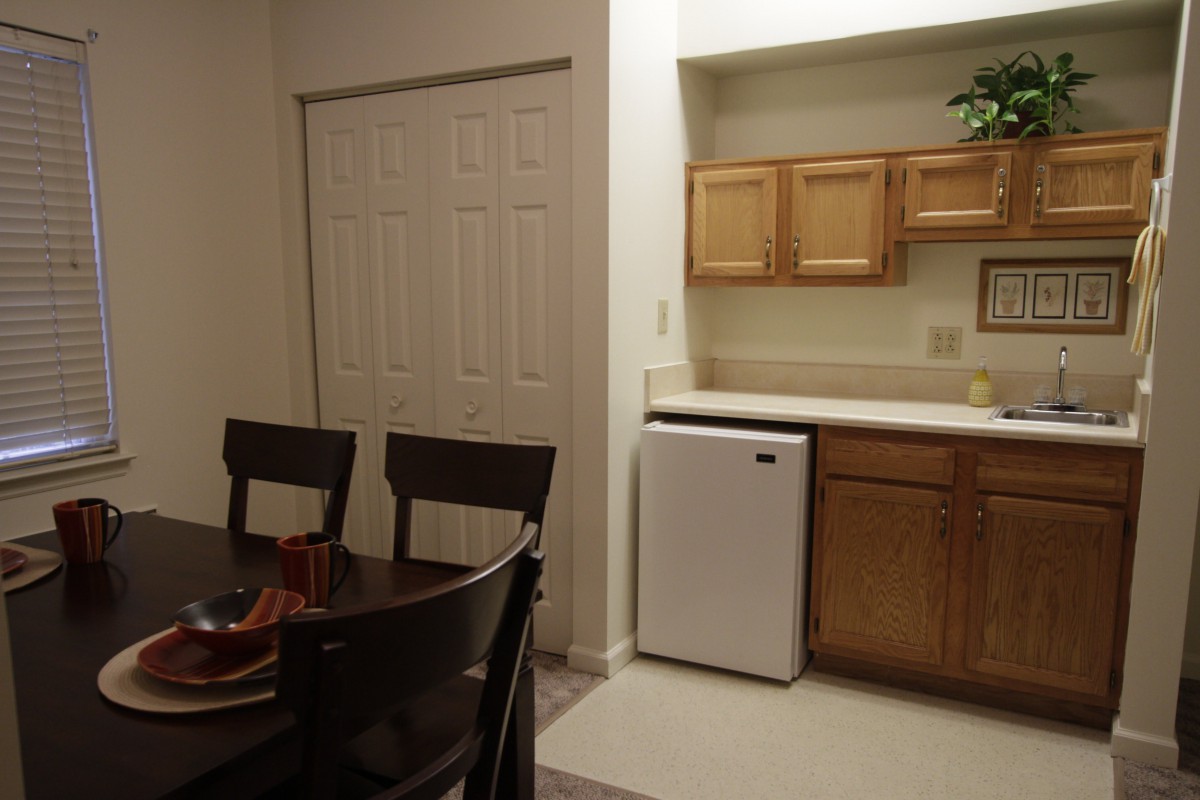 A cozy kitchen and dining area with wooden cabinets, a small refrigerator, and a dining table with chairs.