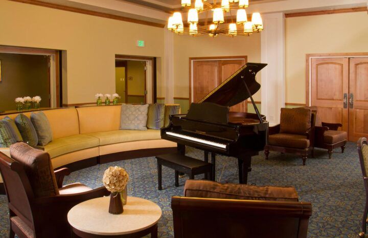 A cozy lounge featuring a grand piano and comfortable seating under a chandelier.