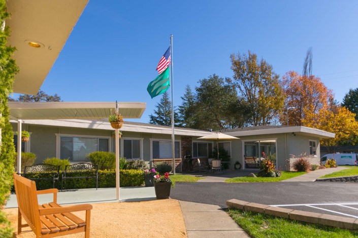 A peaceful courtyard with a building, flagpole, and surrounding greenery under a clear blue sky.