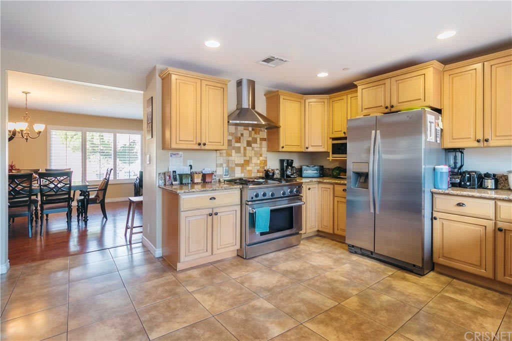 A modern kitchen featuring stainless steel appliances and wooden cabinetry, with an open layout and tile flooring.