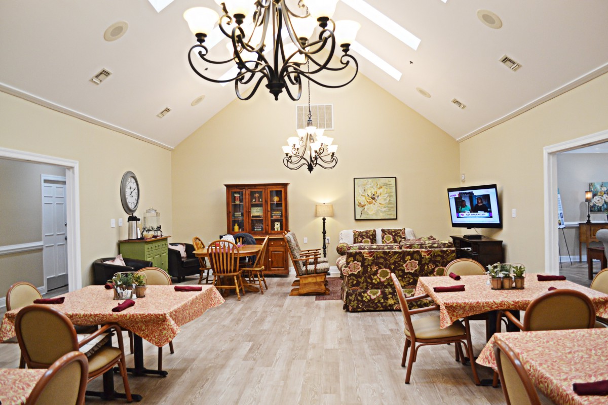 A well-furnished dining room with chandeliers, tables, chairs, a TV, and decorative elements.