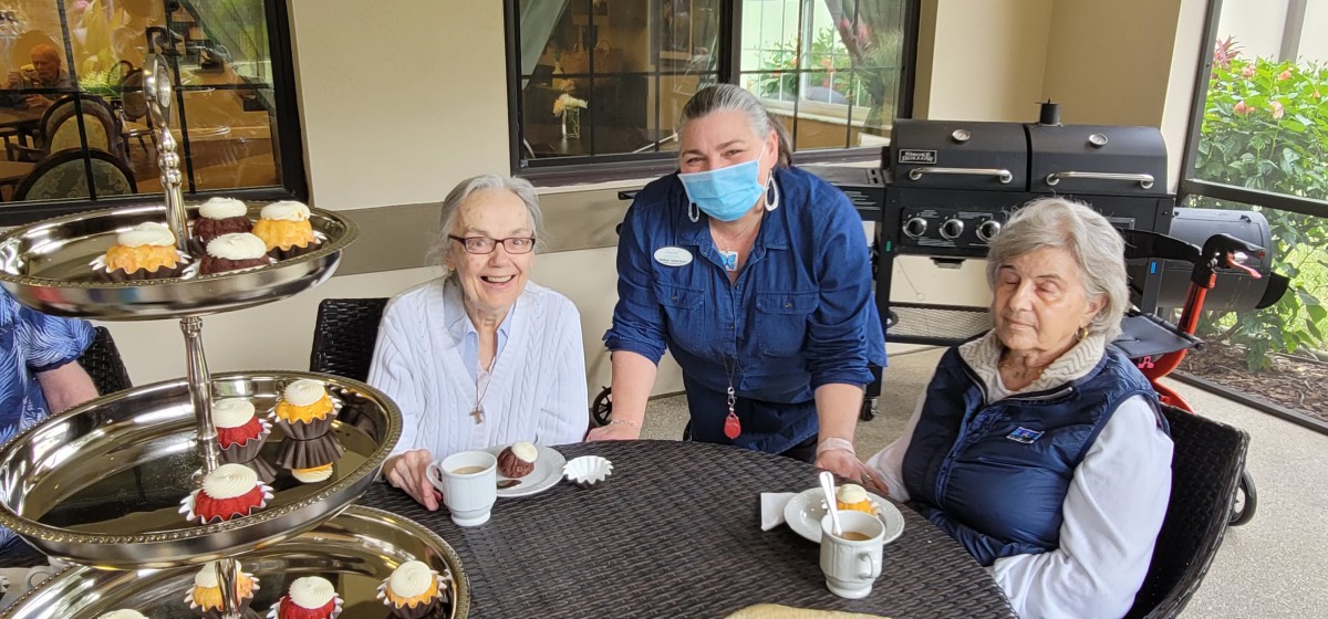 A group of people enjoying coffee and dessert indoors, with one person wearing a mask.