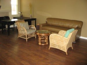 A cozy living room with wicker chairs and a leather couch, featuring a coffee table and wooden flooring.