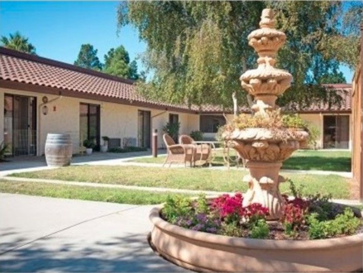 A scenic courtyard with a decorative fountain surrounded by greenery and flowers.