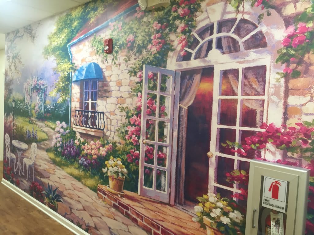 A vibrant mural depicting a charming cottage with abundant floral decorations and an open doorway.