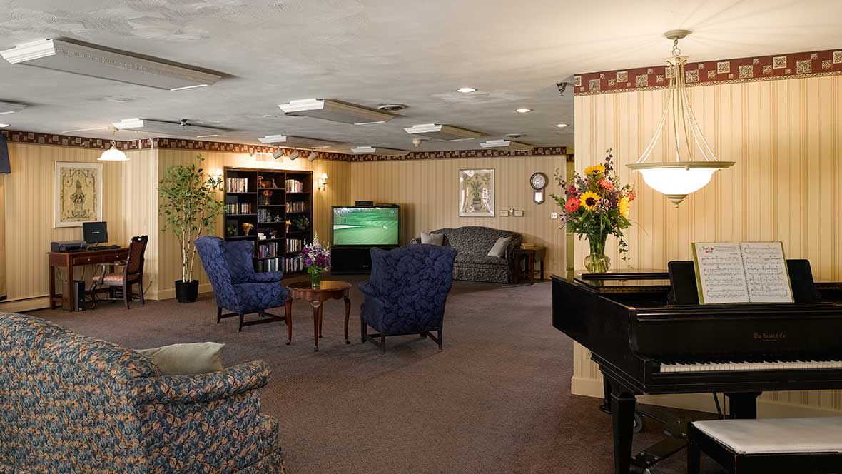 A cozy lounge area with comfortable seating, a television, bookshelves, and a piano.