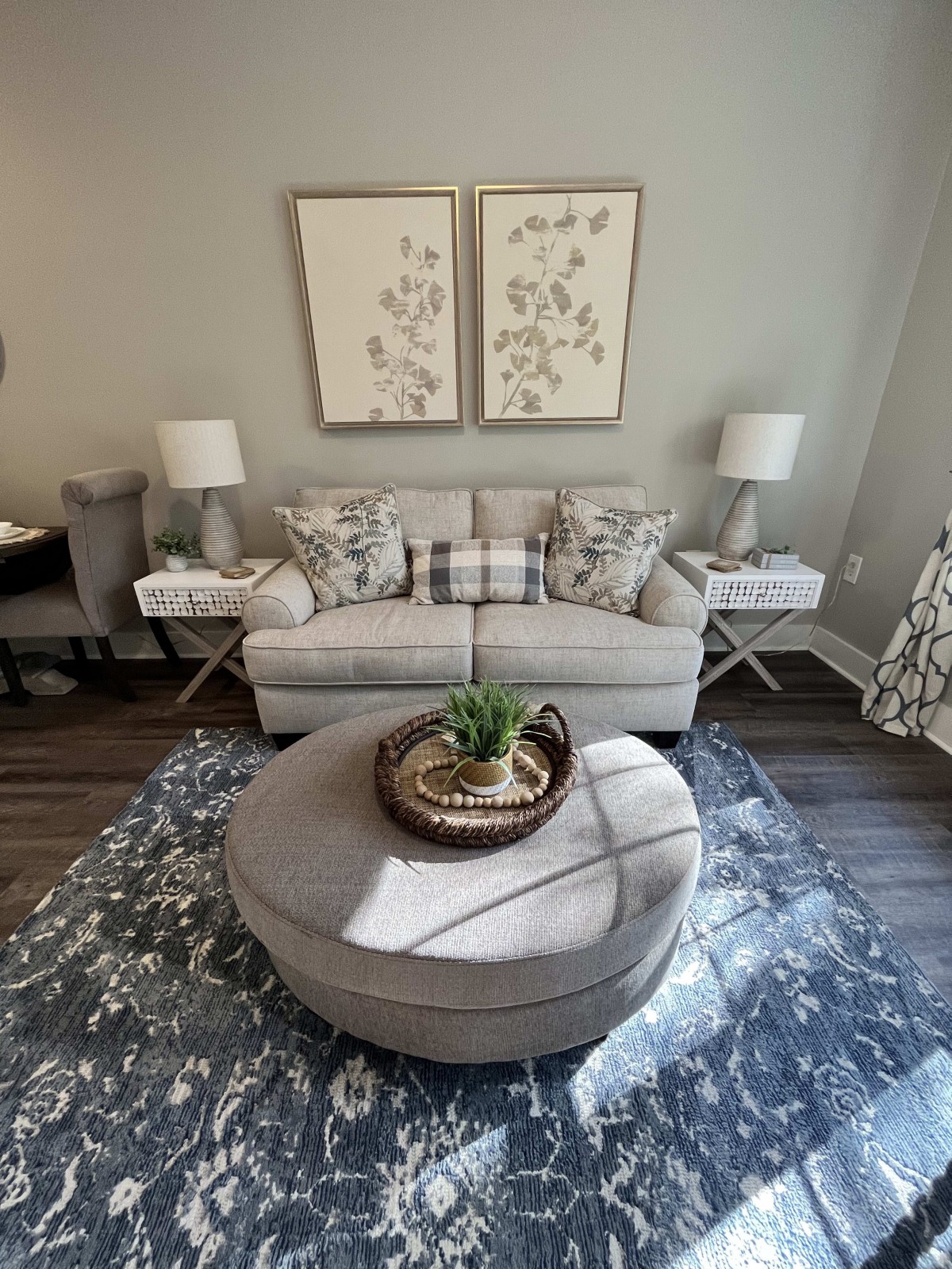 A cozy living room featuring a plush sofa with patterned pillows, flanked by two lamps. An elegant coffee table sits in front, adorned with decorative items, against the backdrop of wall art.