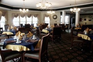 A well-decorated dining area with multiple tables set for a meal, featuring elegant chandeliers and large windows.