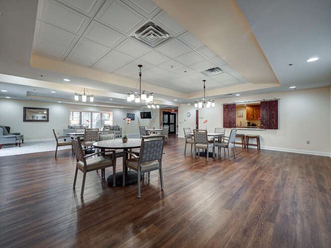 A spacious dining room with modern decor, featuring several tables and chairs, wooden flooring, and elegant lighting fixtures.