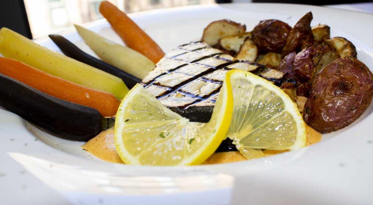 A gourmet plate featuring grilled fish with lemon slices and a side of assorted vegetables.