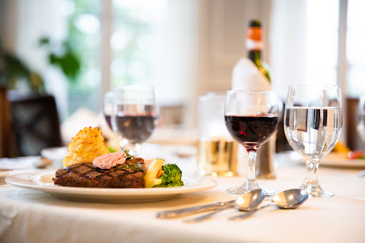 An elegant dining experience featuring a delicious steak, fresh vegetables, and glasses of red wine.