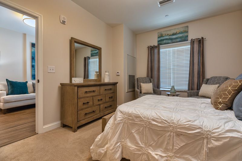 A cozy bedroom featuring a neatly made bed, a wooden dresser with a mirror, and a window adorned with curtains.