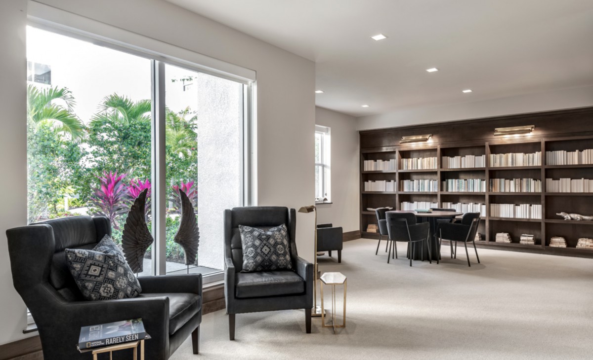 A modern living room with sleek armchairs, a large bookshelf, and ample natural light from the sliding glass doors.