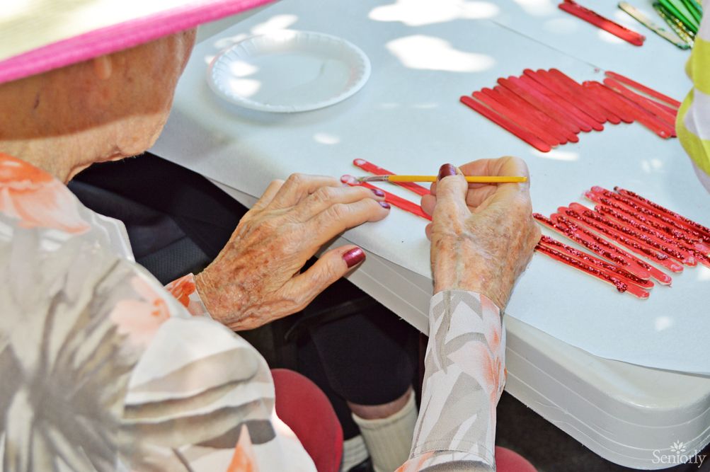 An elderly person engaged in a crafting activity, using a pencil and arranging materials on a table.