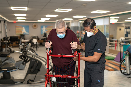 A healthcare professional assists an elderly patient using a walker during physical therapy.