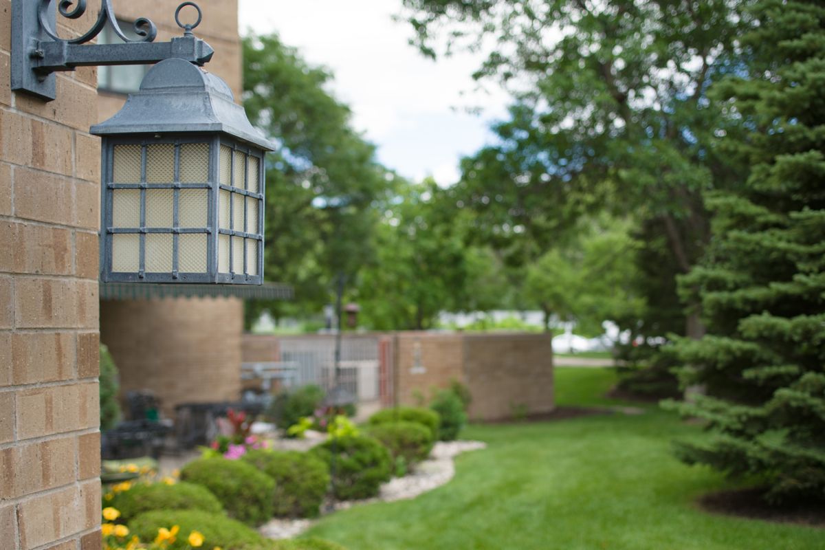 A beautifully landscaped garden with a brick wall and lamp post, surrounded by lush greenery.