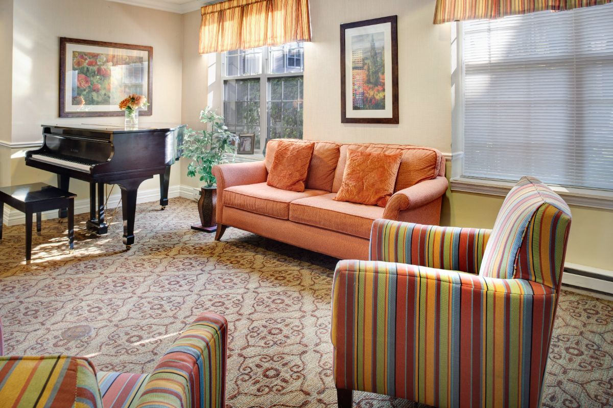 A cozy living room with an orange sofa, striped armchairs, and a piano.