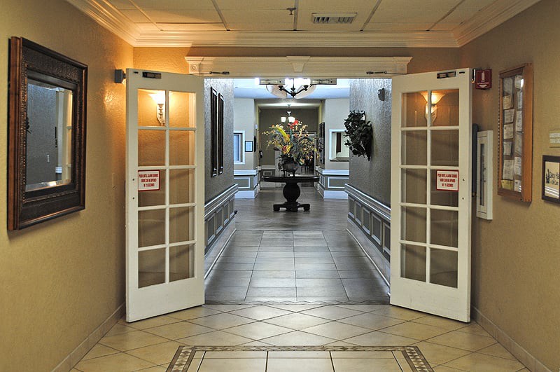 An inviting hallway with open double doors leading to a lobby area, featuring warm lighting and decorative elements.