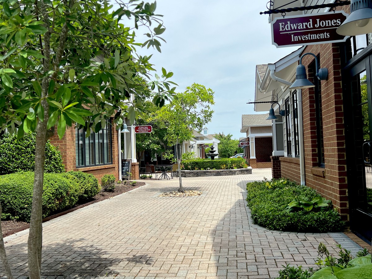 A quaint courtyard with brick buildings and a paved walkway lined with trees and shops.