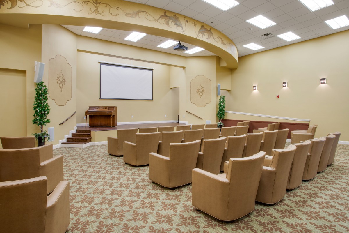 An empty conference room with rows of seats facing a projector screen.