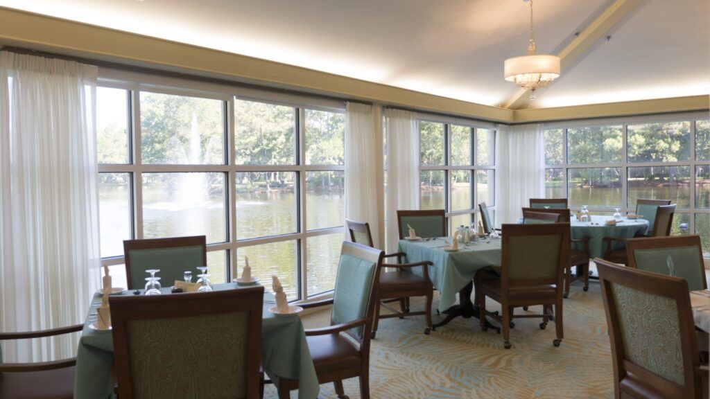 A bright dining room with tables and chairs, featuring large windows that allow natural light to stream in.