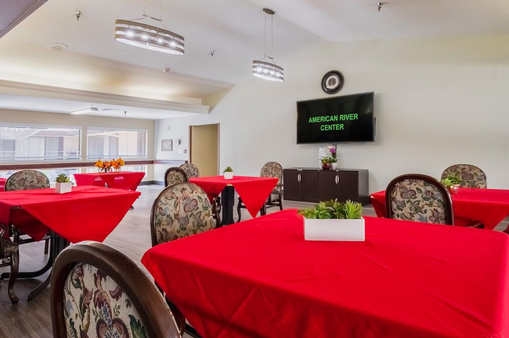 A dining area with red tablecloths, patterned chairs, and a television on the wall.