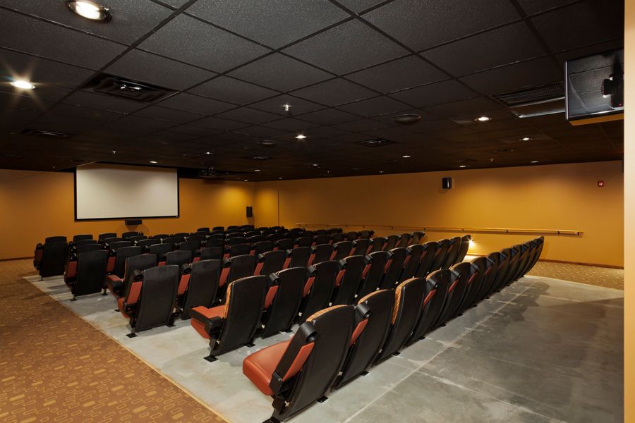 An empty auditorium with rows of seats facing a projector screen.
