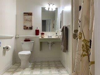 A clean and neatly organized bathroom with a sink, toilet, and mirror.