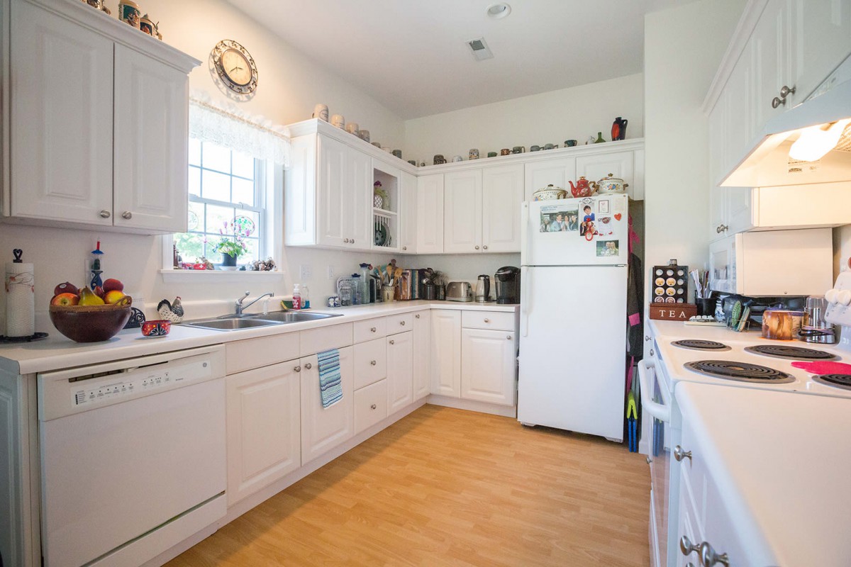 A bright kitchen with white cabinets and a refrigerator, featuring wooden floors and countertop decor.